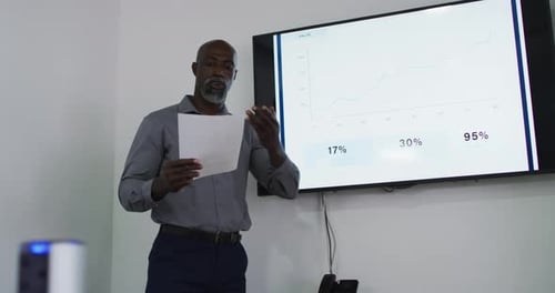 African american businessman talking and pointing at screen, giving presentation in office