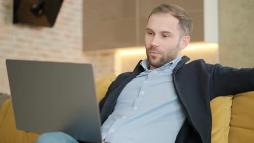 Man Works on Laptop While Relaxing on Couch