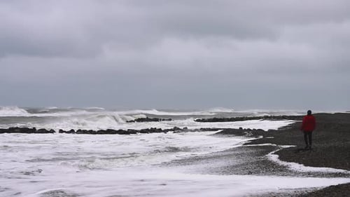 Man Walks By the Sea on a Rocky Coast and Watching Coming Storm and Big Waves