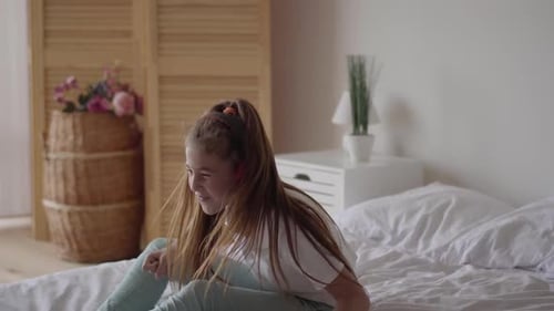 Girl with Headphones Sits on Bed Listening to Music