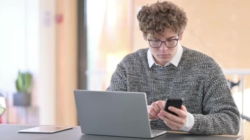 Young Adult Uses Laptop and Smartphone