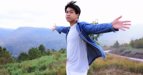 Freedom Asian young man raising hands on the top at the mountain.