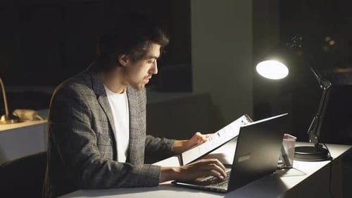 Ein müder Mann schaut sich nachts im Büro einen Finanzbericht auf einem Computer an