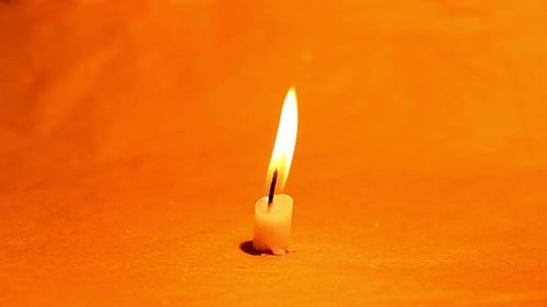 Single Burning Candle Flame on Orange Background