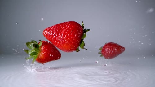 Erdbeeren fallen auf die Wasseroberfläche. Zeitlupe.