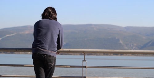 Man Standing Beside a Tranquil Lake on Sunny Day