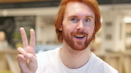 Portrait of Redhead Beard Man Gesturing Victory Sign in Cafe