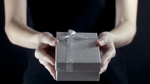 Hands Presenting a Wrapped Gift on Black Background