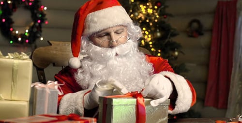 Santa Claus Tying Bow on Christmas Gift at Table