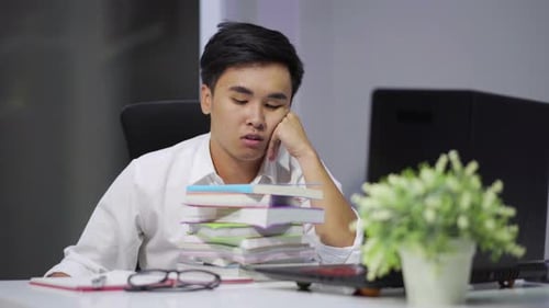 tired student sitting at the table with book and laptop
