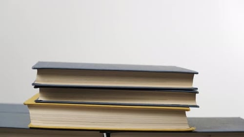 Hand Stacking Colorful Books on a White Surface