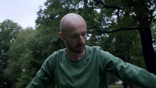Man Does Yoga in the Park in the Middle of a Green Field and Trees