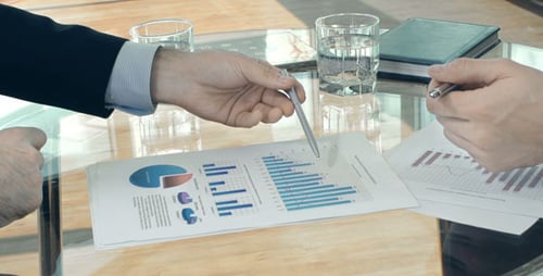 Businessmen Discussing Charts at a Glass Table