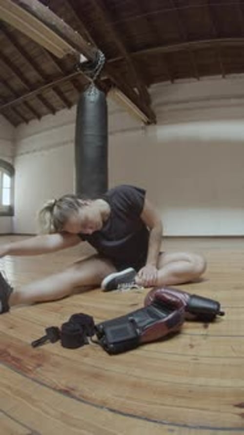 Vertical Shot of Cheerful Female Boxer Stretching in Empty Gym