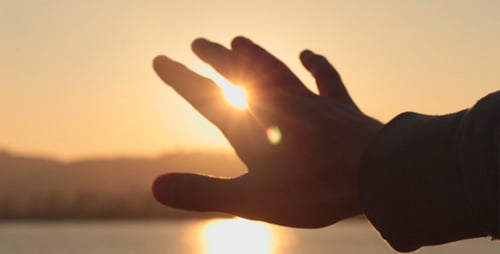 Hand Reaching for the Sun Over the Ocean