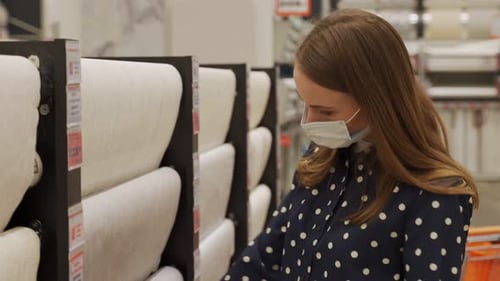 Woman in a Protective Mask Chooses Wallpaper in a Hardware Store