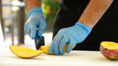 Person Preparing a Mango with Knife on Cutting Board