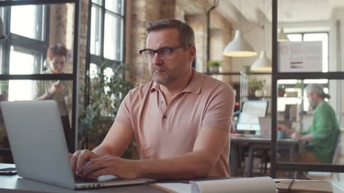 Mature Businessman Typing on Laptop at Office Workplace