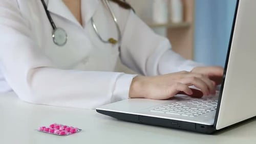 Doctor Works on Laptop with Pills on Desk