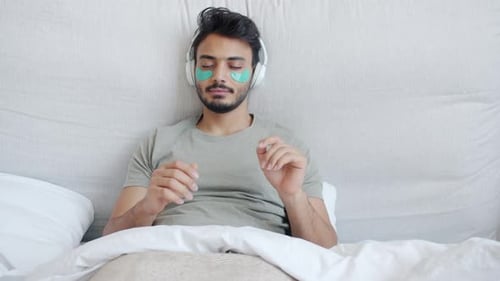 Relaxed Man Wearing Eye Patches and Headphones in Bed