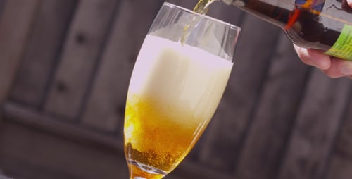 Pouring Frothy Beer into Glass on Sunny Day