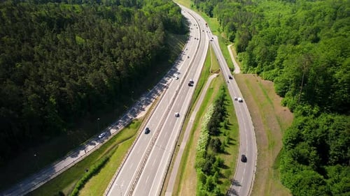 Drone birds eye shot showing traffic on asphalt highway surrounded by green dense woodland