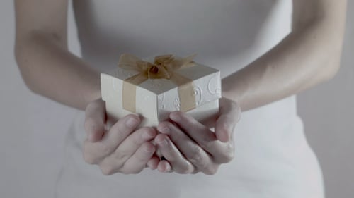 Woman Presents Small Gift Box with Gold Bow