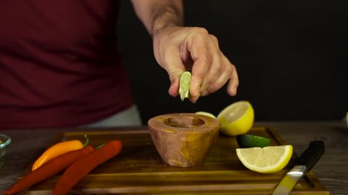 Man Squeezing Lime into Wooden Bowl with Peppers