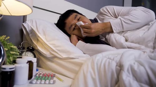 Man Blowing Nose in Bed at Night