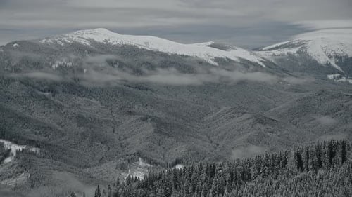 Scenic Winter Landscape in the Mountains with Clouds Above and Below and Woods Covered in Snow