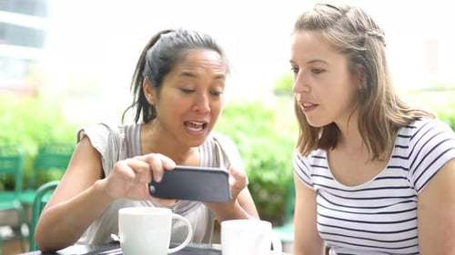 Friends looking at smartphone together in outdoor cafe
