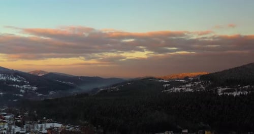Luftaufnahme von schneebedeckten Bergen und Wäldern bei Sonnenuntergang im Winter