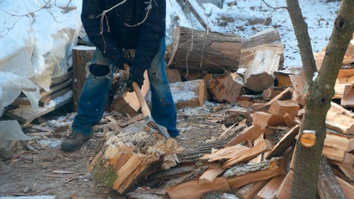 Man Chopping Wood with Axe on Winter Day