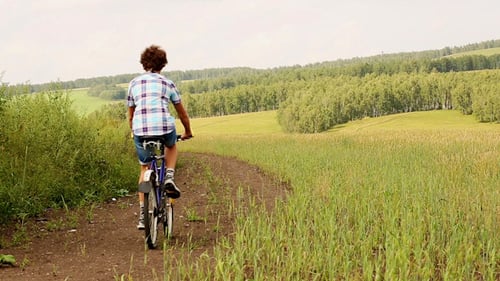 Teen Rides Bike Through Green Rural Meadow