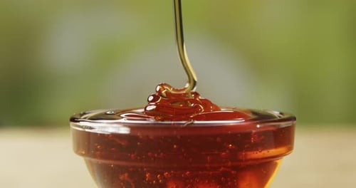 Yellow Honey Is Pouring Down Into A Small Glass Bowl On A Green Background
