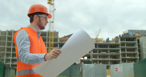 Young Architect or Builder With Hard Hat Holding Blueprint In His Hands in Front of Building Under