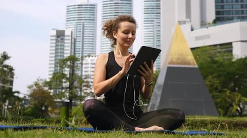 Young Woman Exercising At Park Doing Yoga Using Tablet Computer