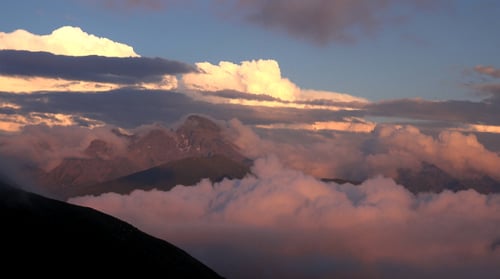 Sunset over Majestic Mountain Peaks Surrounded by Clouds