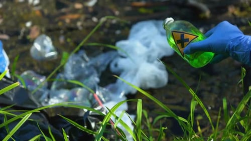 Gloved Hand Holding Toxic Liquid Near Plastic Trash