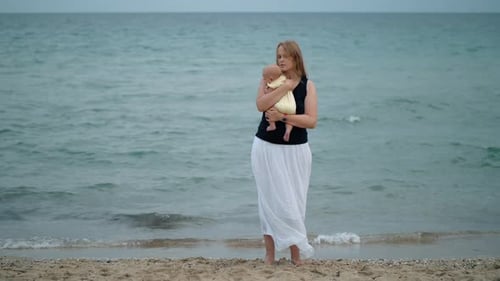 Mother cuddling baby, scene at the beach against the sea