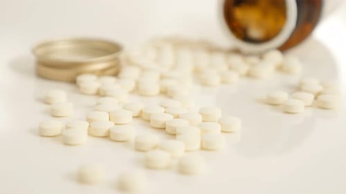 White Pills Scattered with Medicine Bottle on White Surface