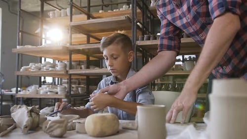 Boy Sculpting Clay with Assistance in Pottery Studio