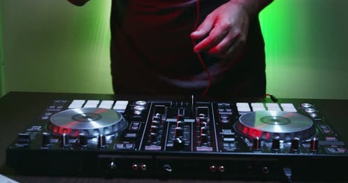 DJ Adjusting Mixer in Green Lit Room