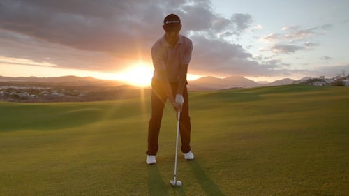 Golfer Swings Club on Green at Sunset