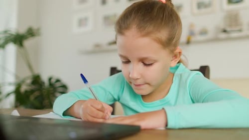 Young Girl Writing at Table Indoors During Daytime