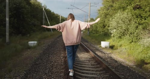 Junge einsame Frau geht die Eisenbahnstrecke entlang und balanciert auf einer Schiene