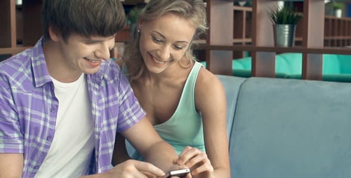 Smiling Couple Looking at Smartphone in Cafe Together