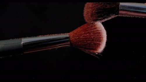 Dos pinceles de maquillaje con polvo sobre fondo negro con luz solar, concepto de pintura a cámara lenta