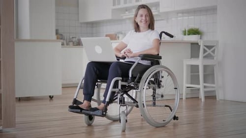 Woman Smiling with Laptop in Wheelchair at Home