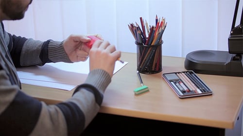 Man Sharpens Pencil at Desk with Art Supplies